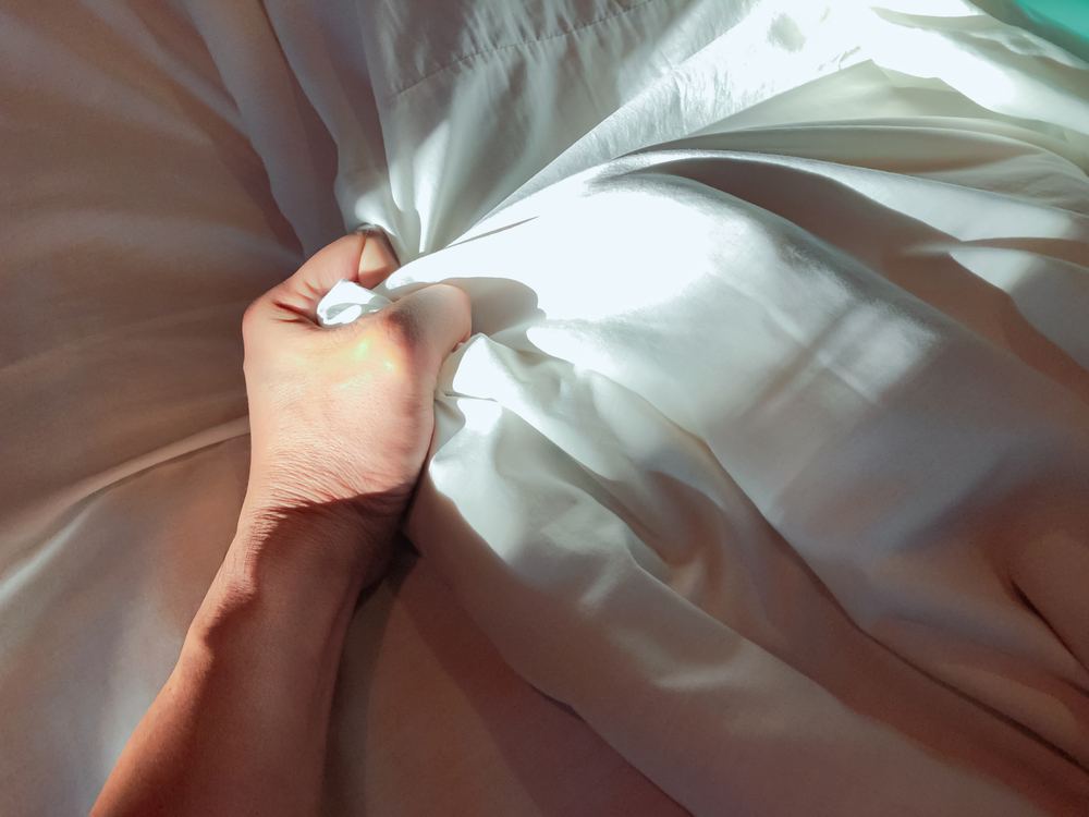 Male orgasm and sexual pleasure: hand gripping white bed sheets during intimacy