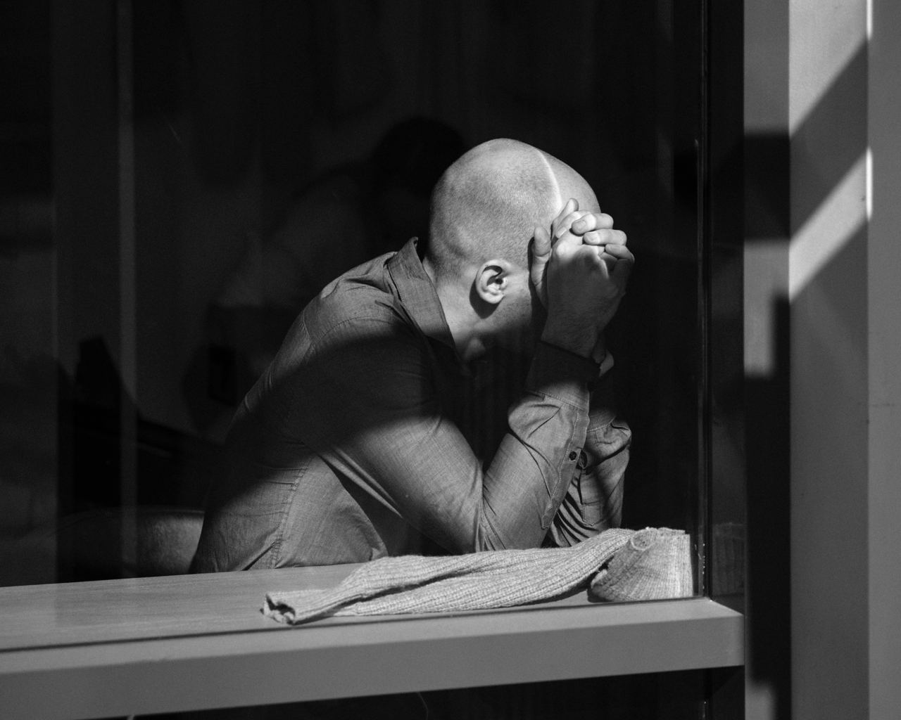 Мужчина сидит у окна, закрыв лицо руками - депрессия у мужчин, эмоциональное выгорание и признаки психологического кризиса