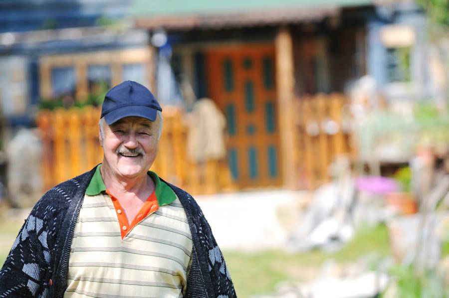 Smiling man over 40 standing near a country house, symbolizing active aging, men’s health, and life after andropause