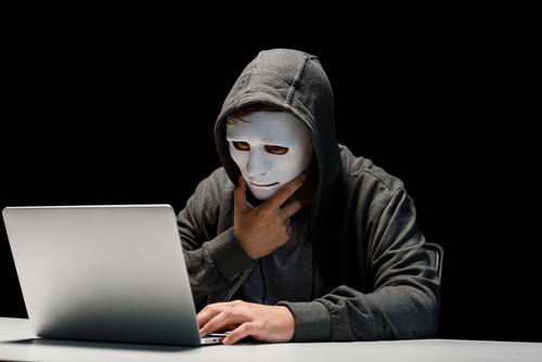 Teenager in a mask and hoodie using a laptop, illustrating anonymity, digital addiction, and the impact of social media on adolescent mental health